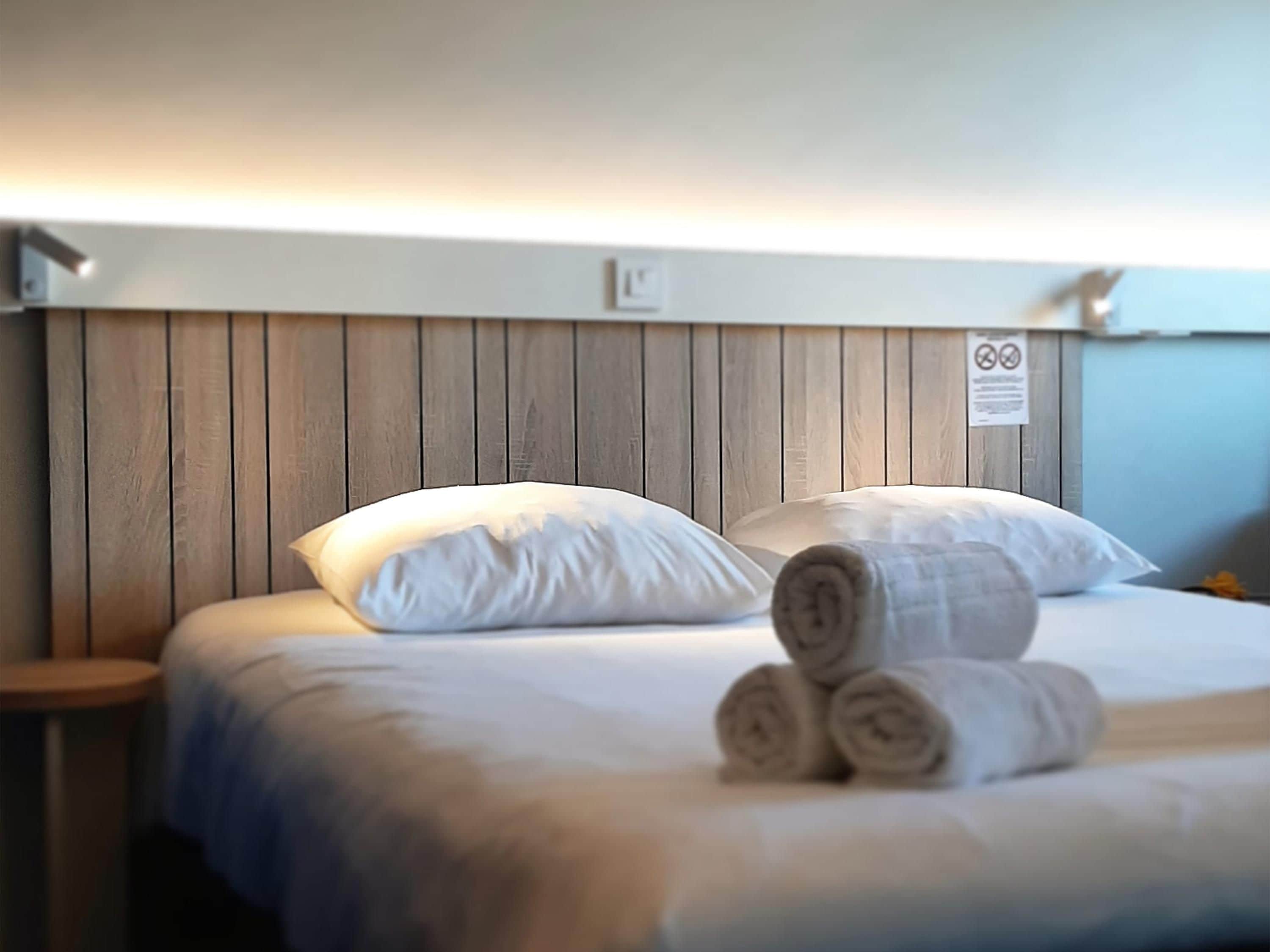 Una habitación de hotel con cabecera de madera, ropa de cama blanca y toallas enrolladas sobre la cama.