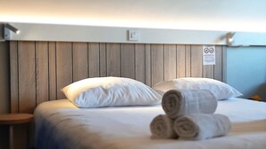 A hotel room with a wooden headboard, white bedding, and rolled towels on the bed. - ibis Rennes Cesson (Cesson-Sevigne)