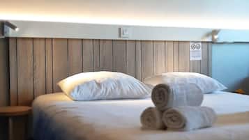 Una habitación de hotel con cabecera de madera, ropa de cama blanca y toallas enrolladas sobre la cama.