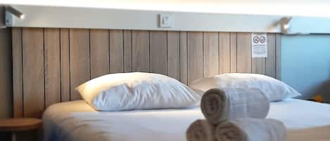 A hotel room with a wooden headboard, white bedding, and rolled towels on the bed.