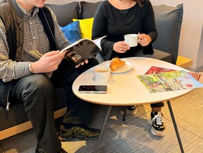 Dos personas sentadas en una mesa redonda con un teléfono inteligente, una taza de café y un croissant.