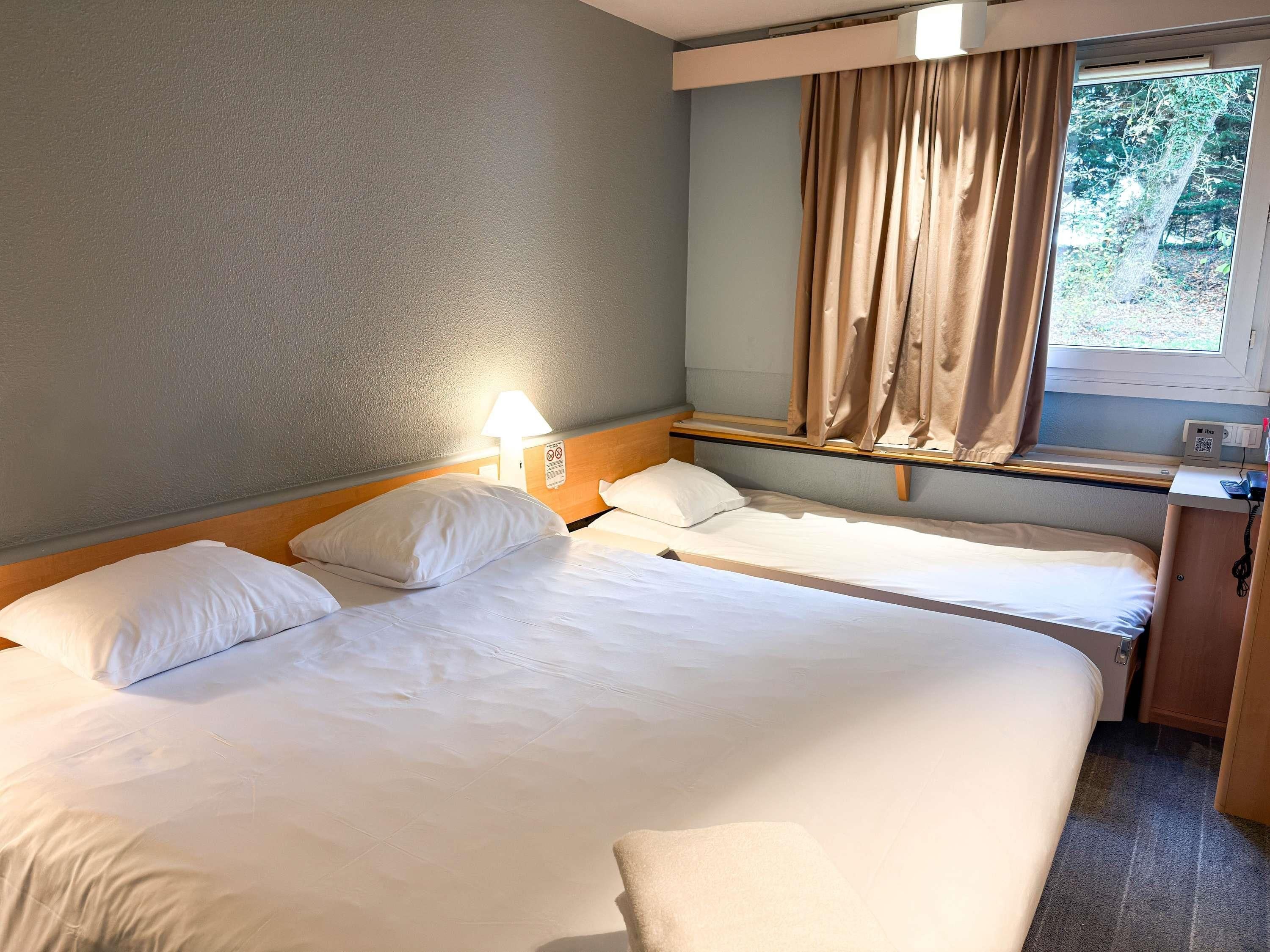 Habitación de hotel con una cama grande, una mesita de noche, una lámpara y una ventana con cortinas.