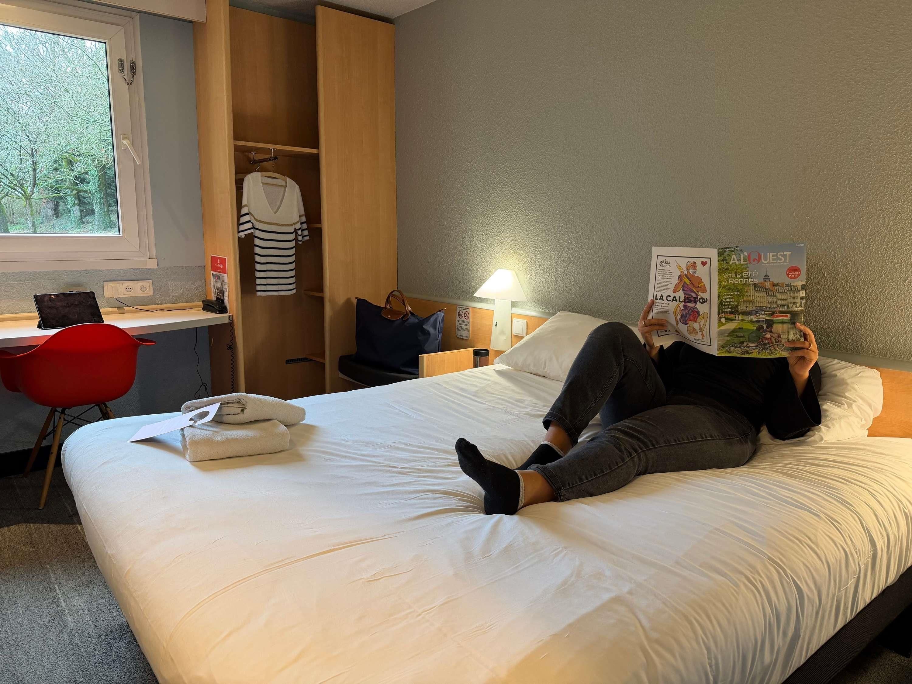 A hotel room with a bed, a desk, a chair, and a wardrobe.