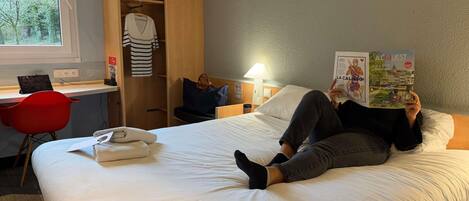 A hotel room with a bed, a desk, a chair, and a wardrobe.