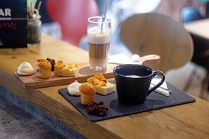 Una mesa con una taza negra, un vaso de café helado y varios pasteles.