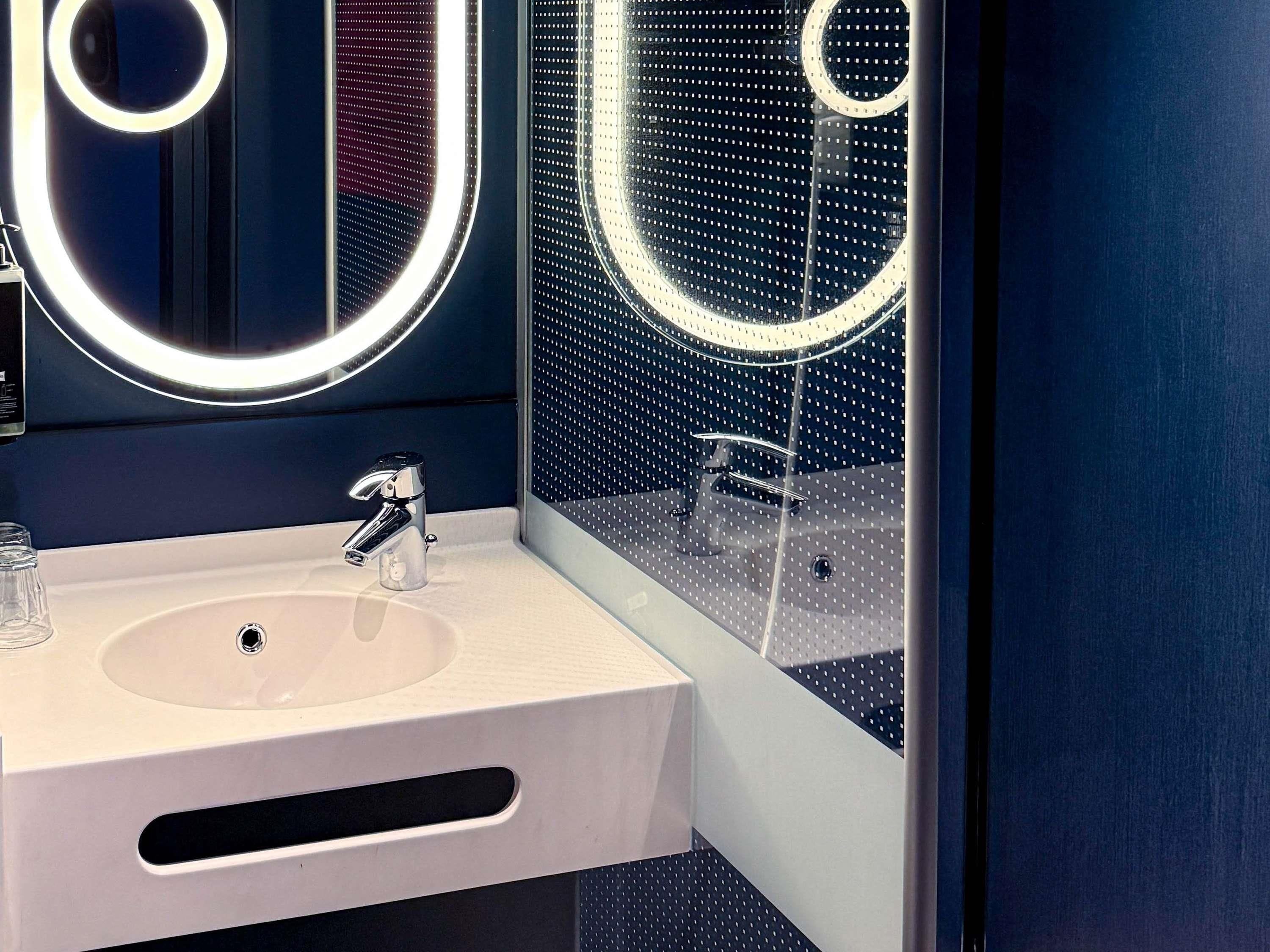 A modern bathroom with a white sink, chrome faucet, and a large mirror with circular light fixtures.