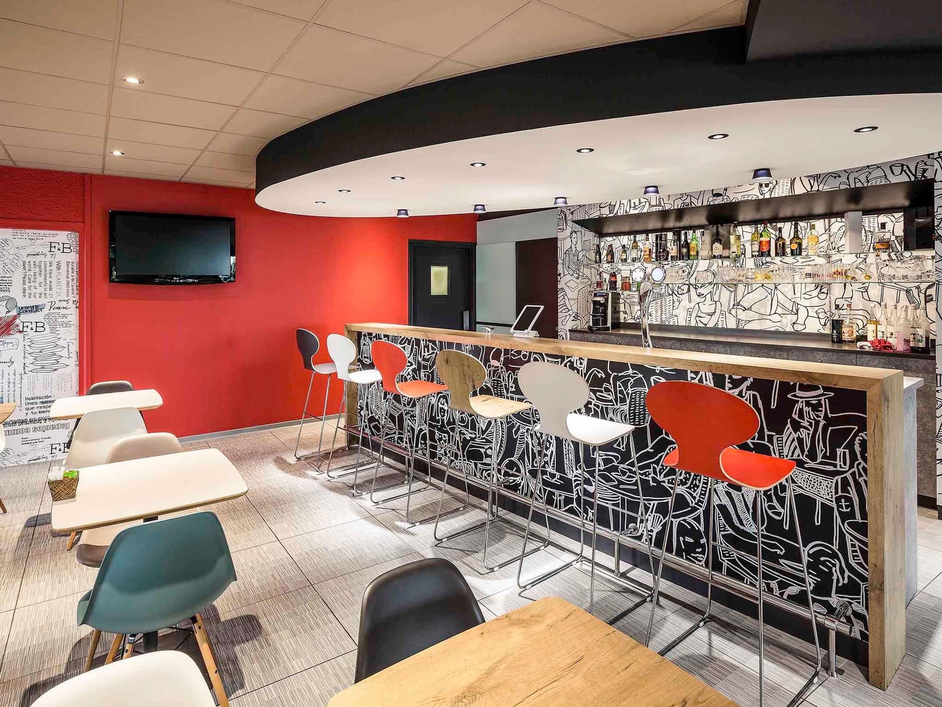 Un espace bar doté d’un comptoir incurvé, de différents types de sièges, notamment des chaises et des tables, et d’un mur orné d’un motif abstrait en noir et blanc.