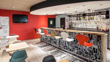 Eine Bar mit einer gebogenen Theke, verschiedenen Sitzmöglichkeiten, darunter Stühle und Tische, sowie einer Wand mit einem schwarz-weißen abstrakten Muster.