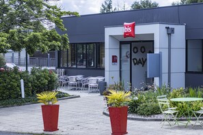 Una entrada de hotel moderna con un letrero rojo, asientos exteriores y plantas en macetas.