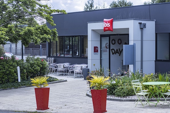 Una entrada de hotel moderna con un letrero rojo, asientos exteriores y plantas en macetas.