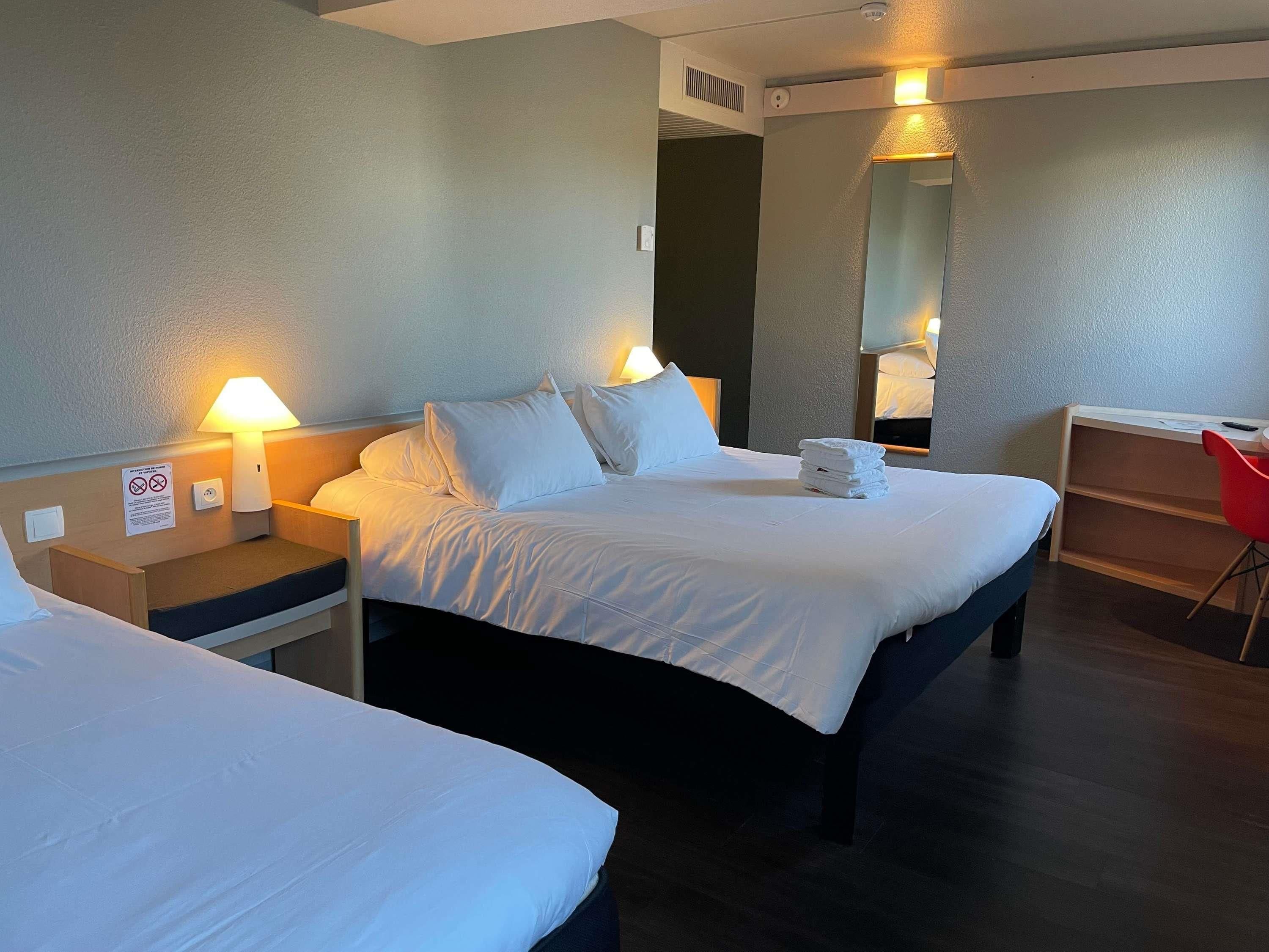 A hotel room with two beds, a desk, a chair, and a mirror.