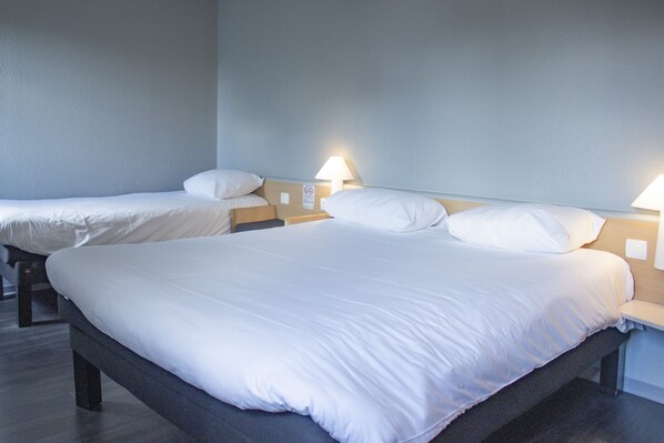 A hotel room with two single beds, each with a nightstand and a lamp. - ibis Rennes Cesson (Cesson-Sevigne)