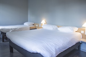 Quarto de hotel com duas camas de solteiro, cada uma com mesa de cabeceira e luminária.
