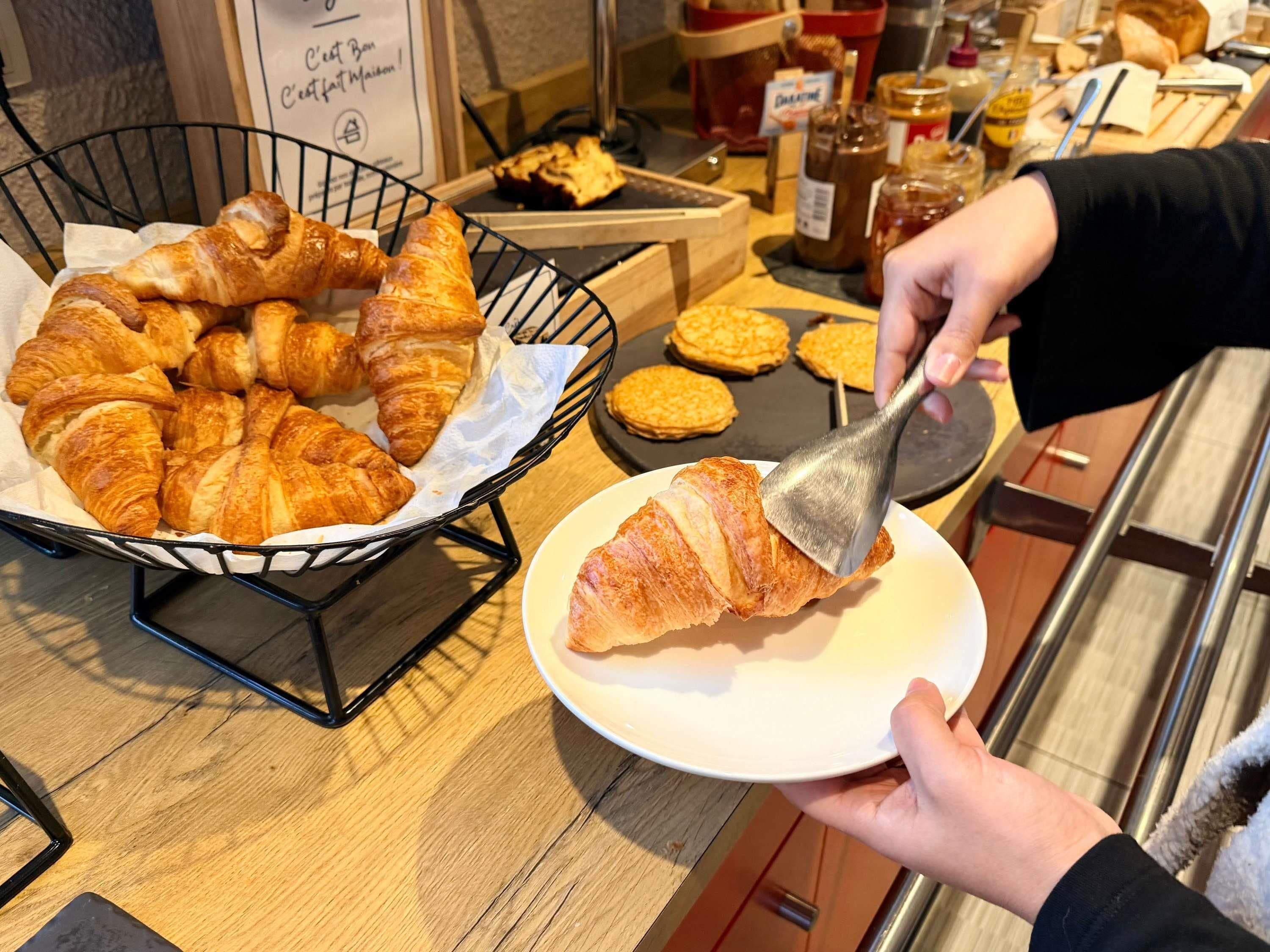 A basket of croissants on a wooden counter with a sign in the background.