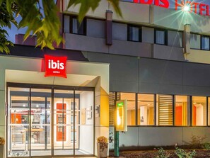 A hotel entrance with a red sign, glass doors, and a reception area visible inside. - ibis Rennes Cesson (Cesson-Sevigne)