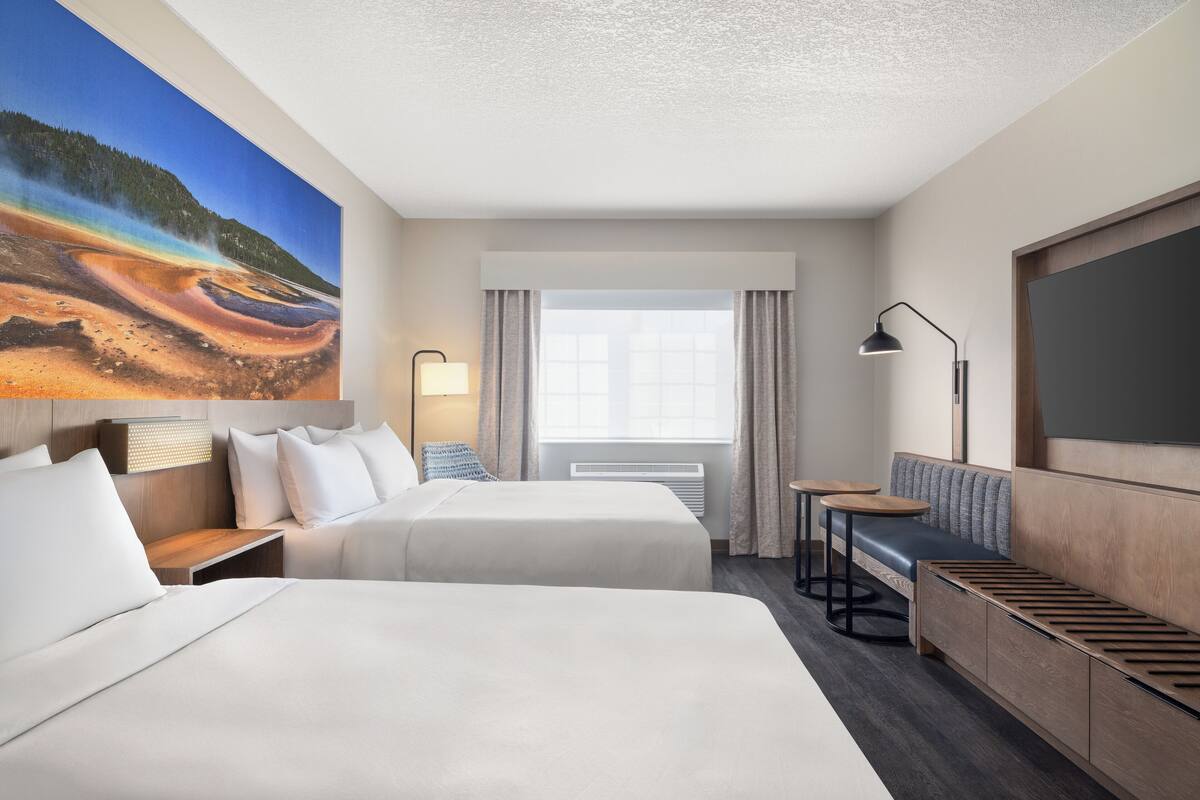 A hotel room with two beds, a sofa, a small table, and a painting of a natural landscape.