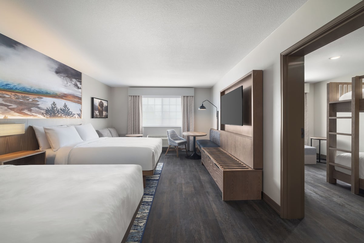 A modern hotel room with two beds, a seating area, a TV, and a large window.