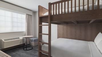 Ein Stockbett mit Holzrahmen und weißer Bettwäsche, ein runder Tisch mit schwarzem Gestell, ein eingebauter Heizkörper und ein Fenster mit Vorhängen.