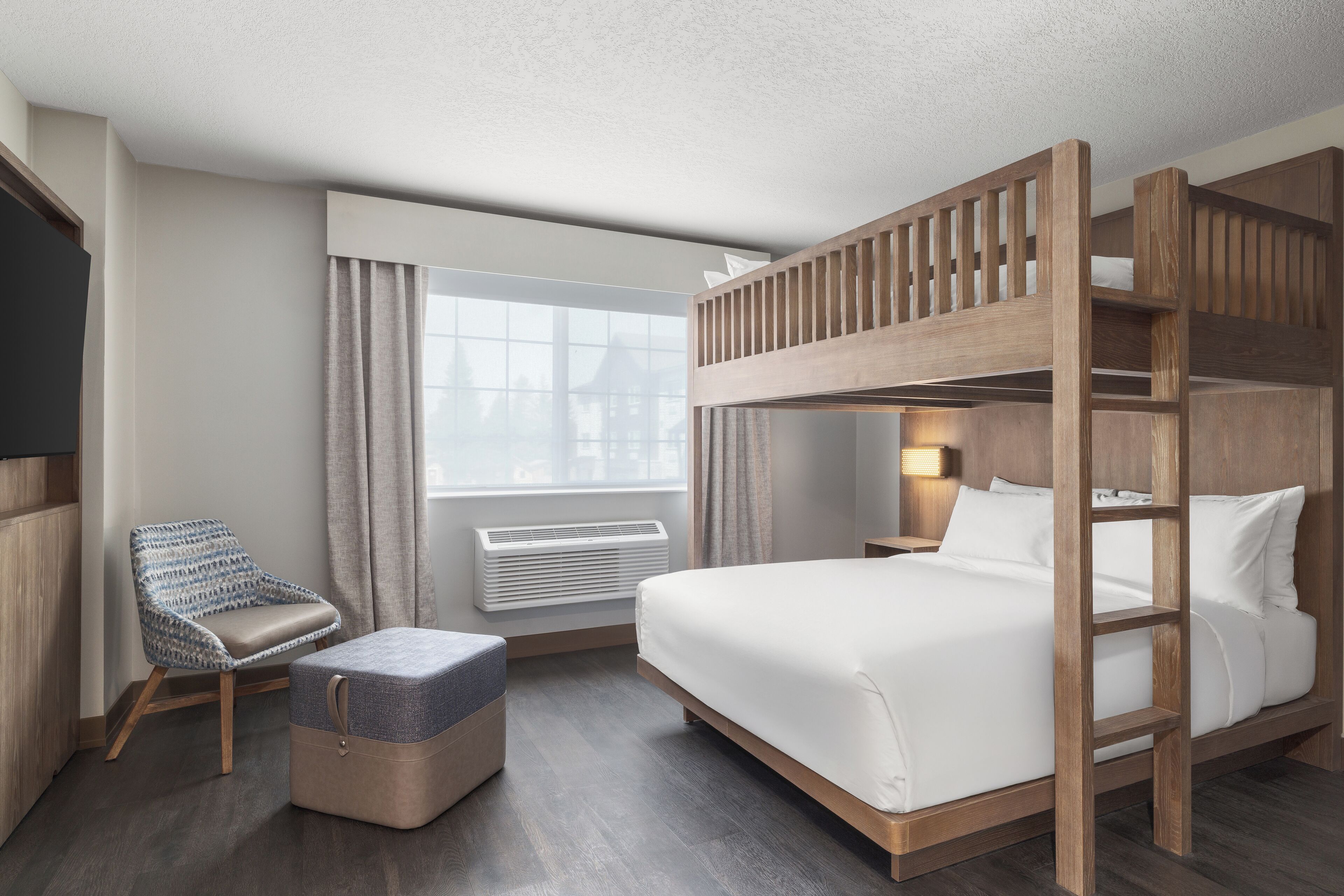 A hotel room with a bunk bed, a single bed, a chair, and a small table.