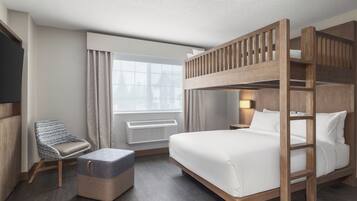 A hotel room with a bunk bed, a single bed, a chair, and a small table.