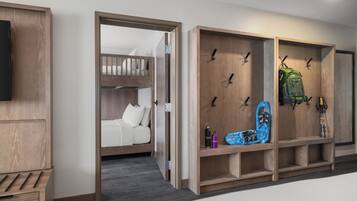 Una habitación de hotel moderna con una cama litera, un armario de madera con ganchos y un televisor montado.
