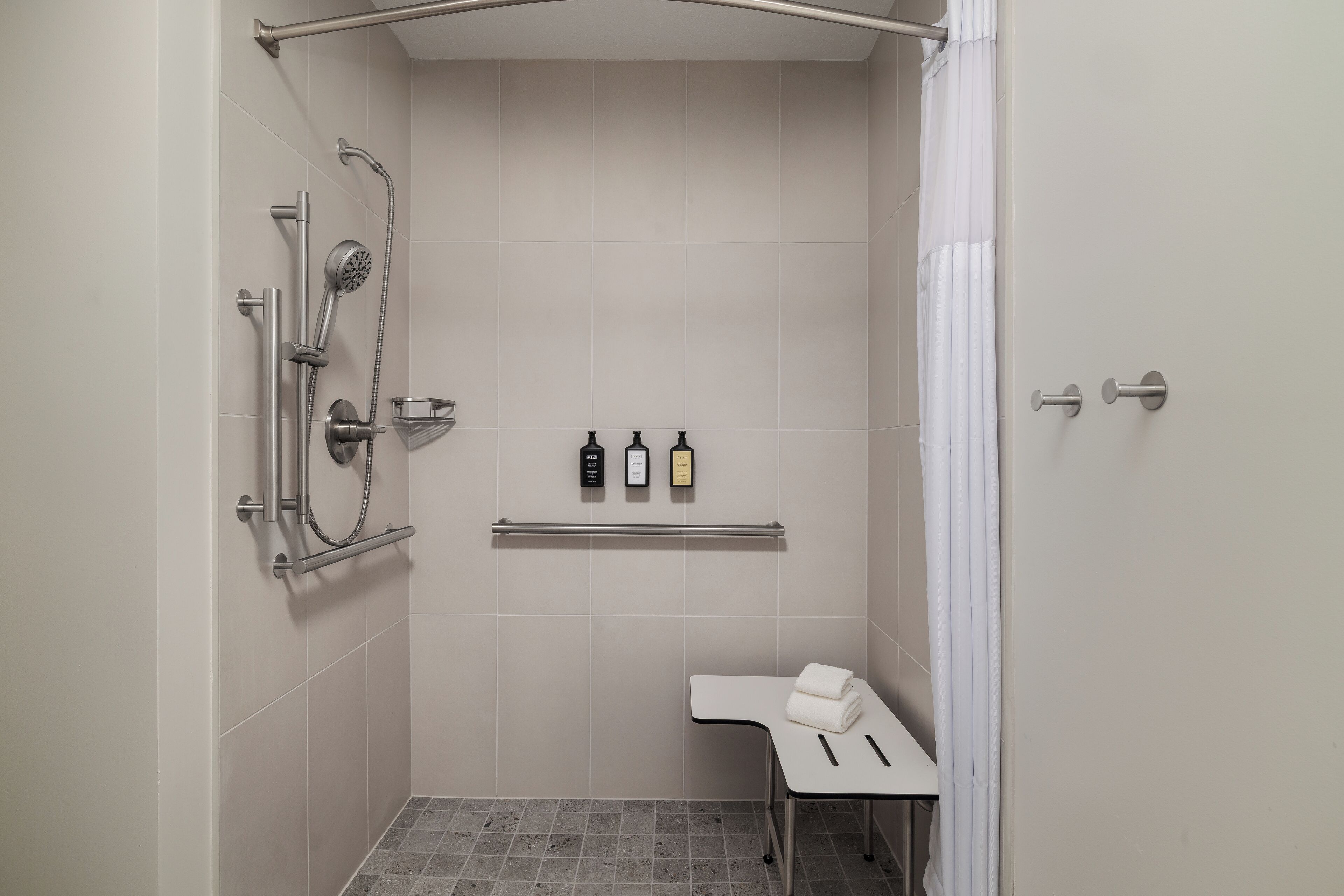 A modern bathroom with a shower, a towel rack, and a shelf with toiletries.