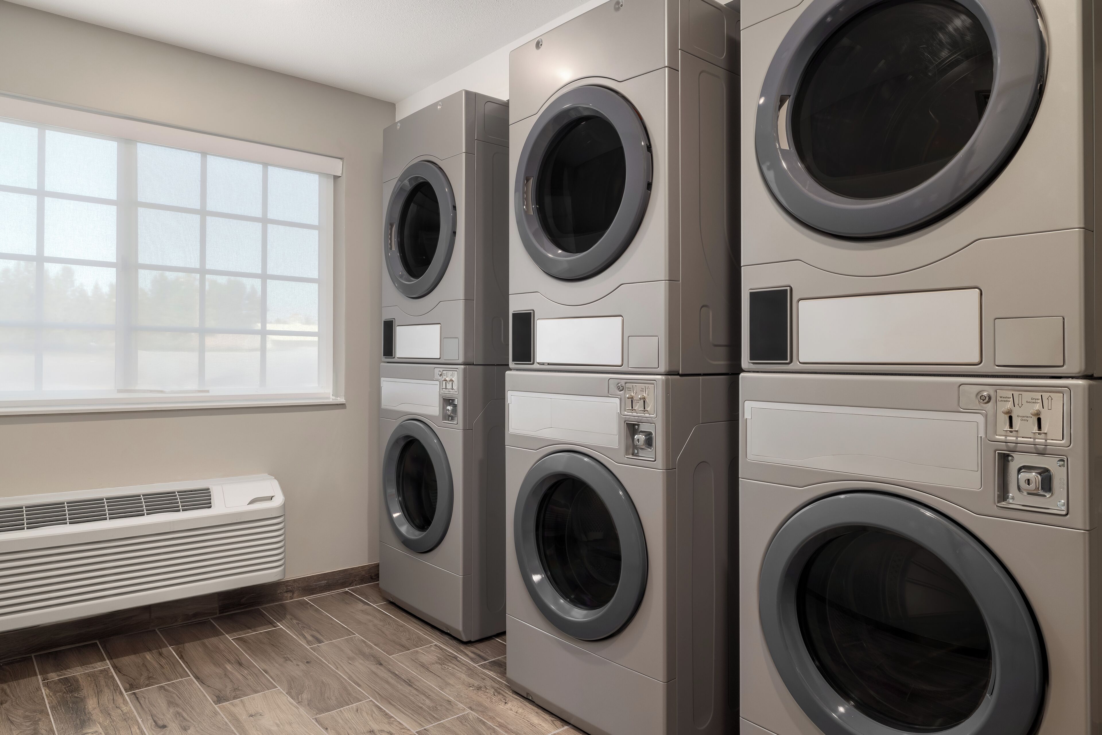 A laundry room with four stacked front-loading washing machines, a window, and a wall-mounted air heater.