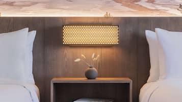 A hotel room with a bed, a bedside table with a vase and books, and a wall-mounted light fixture.