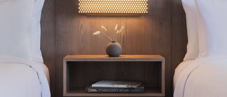 A hotel room with a bed, a bedside table with a vase and books, and a wall-mounted light fixture.