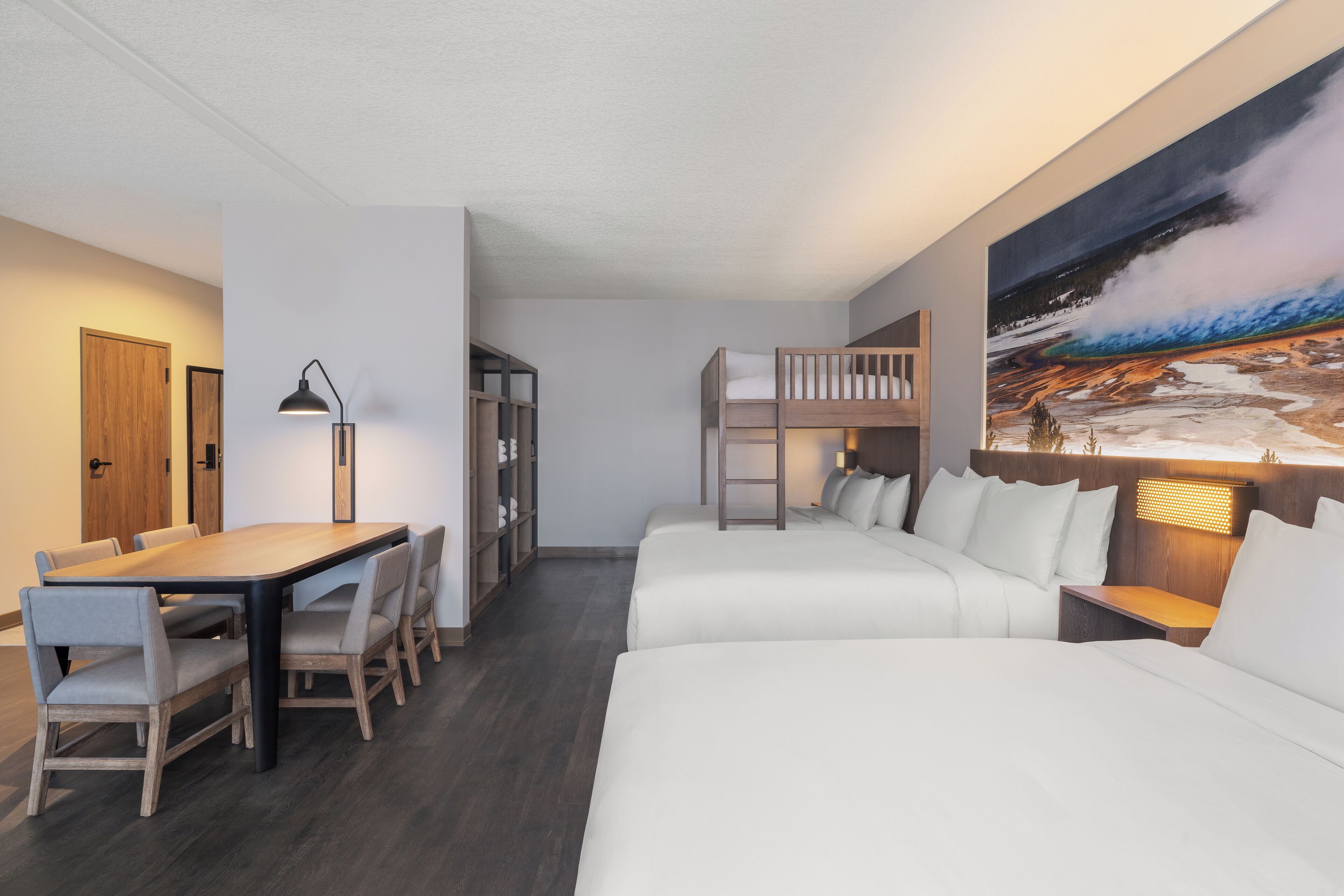 Una habitación de hotel con literas, una mesa de comedor con sillas, una estantería y un cuadro grande en la pared.