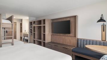 Una habitación de hotel moderna con una cama grande, armario empotrado, zona de estar con un banco y un televisor de pantalla plana montado en la pared.