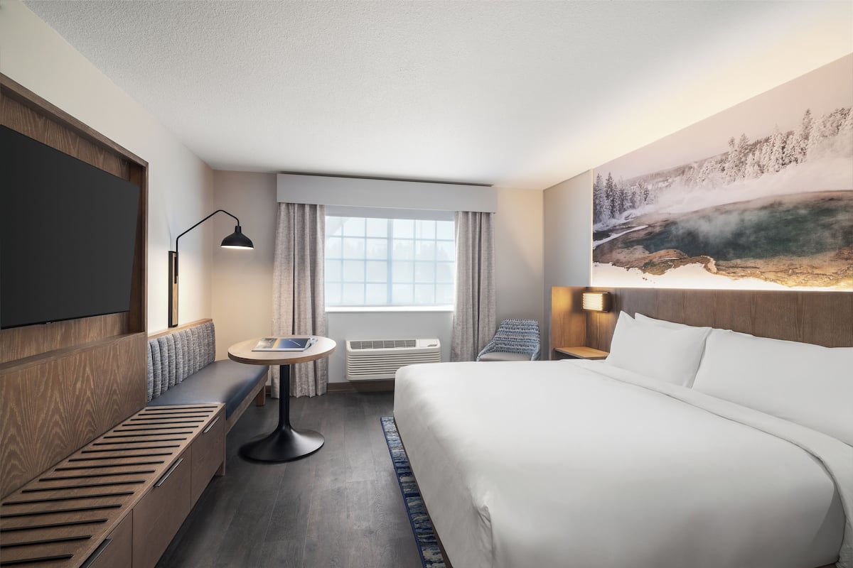 A hotel room with a large bed, a seating area with a table, a flat-screen TV, and a painting of a landscape.