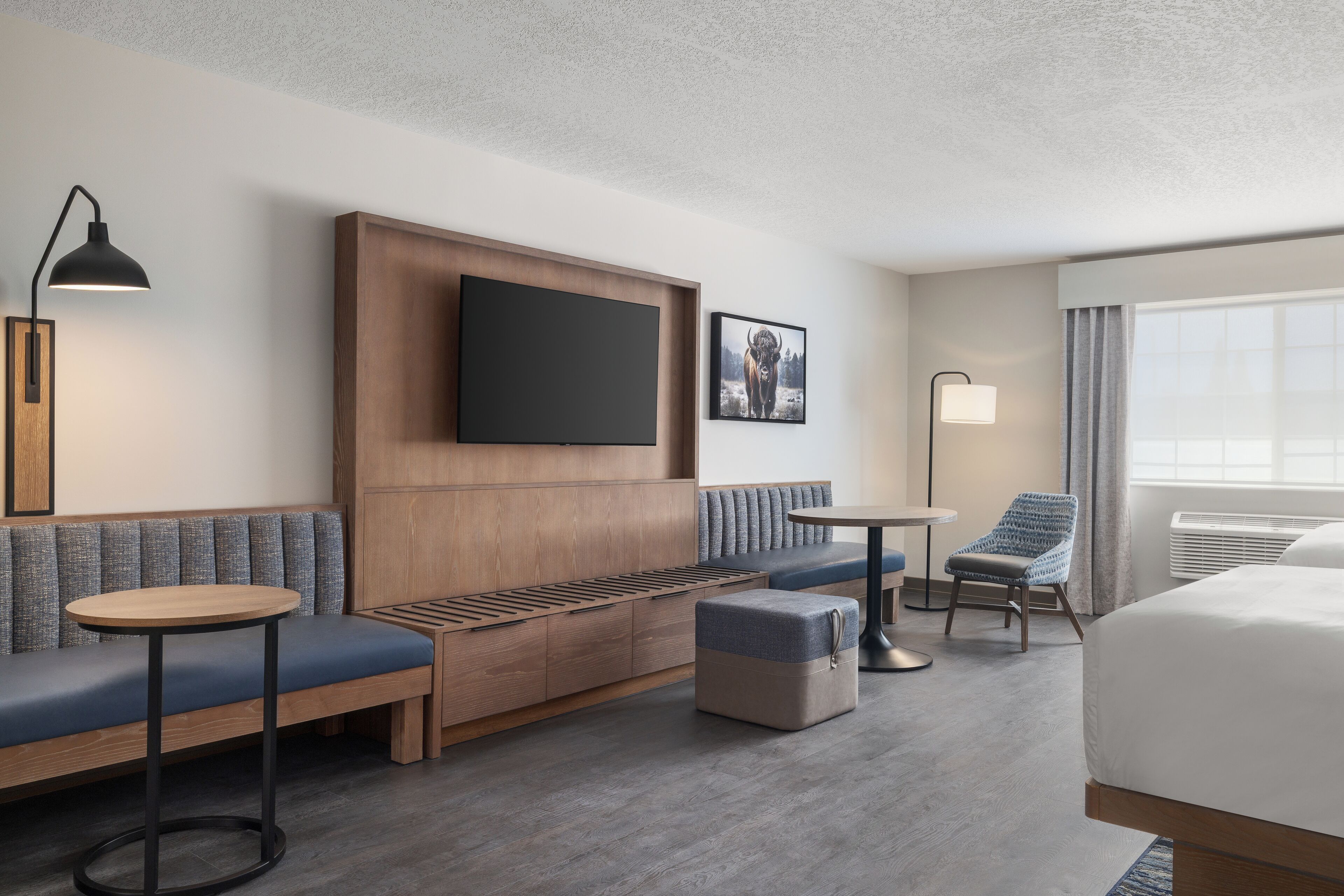 Une chambre d’hôtel avec un mur lambrissé en bois, un téléviseur à écran plat, un canapé, une petite table ronde, une chaise et un lit.