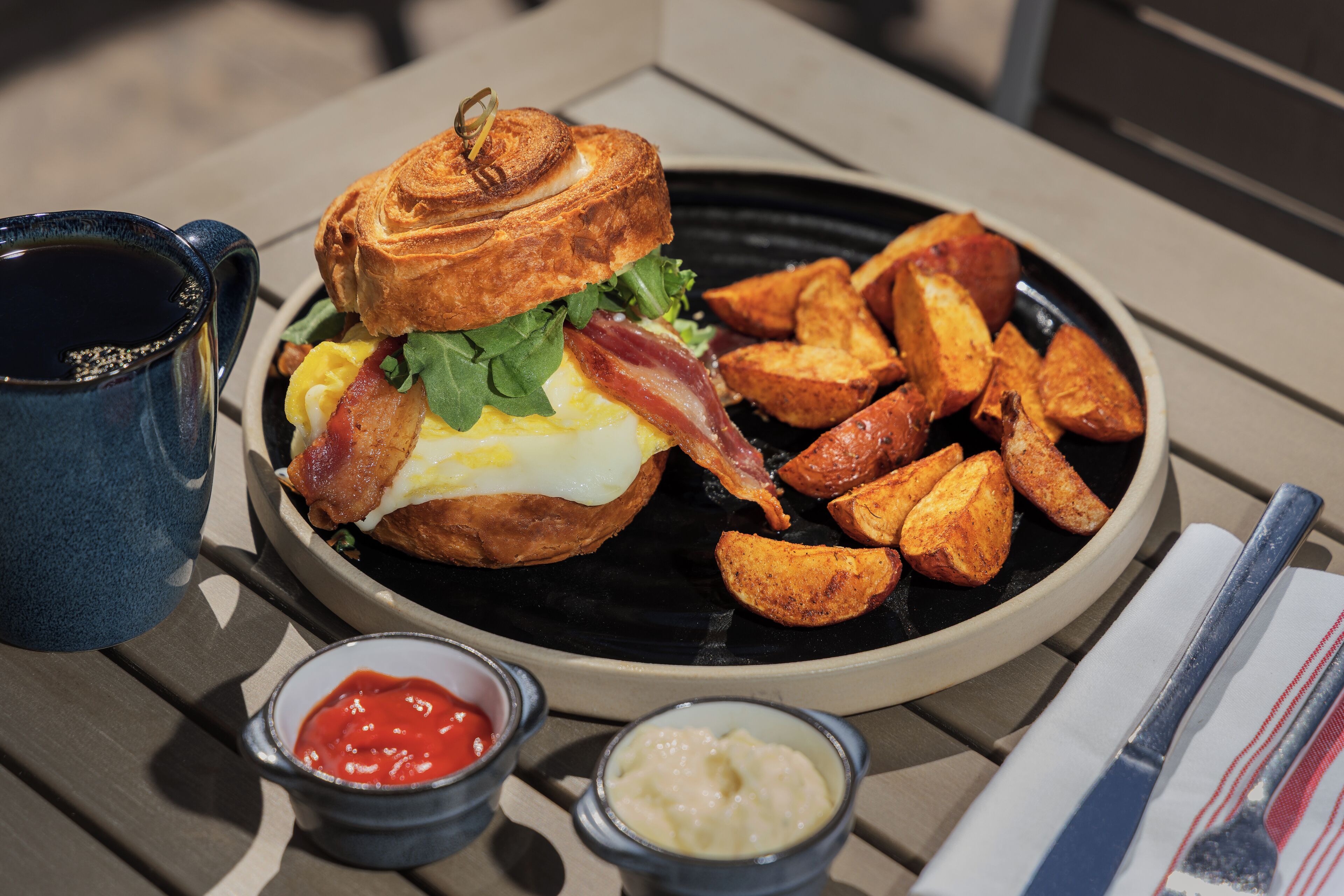 Un plato de comida con un sándwich, papas fritas y dos recipientes pequeños de salsas.