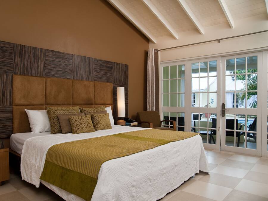 A bedroom with a large bed, a wooden headboard, two bedside tables, and a view through a glass door.