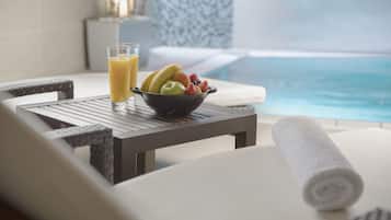 Ett matbord med en skål med frukt och ett glas apelsinjuice, en hoprullad handduk och utsikt över en pool.