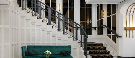 Un grand escalier avec une rampe noire, menant à un palier où se trouvent un canapé vert et une table basse.