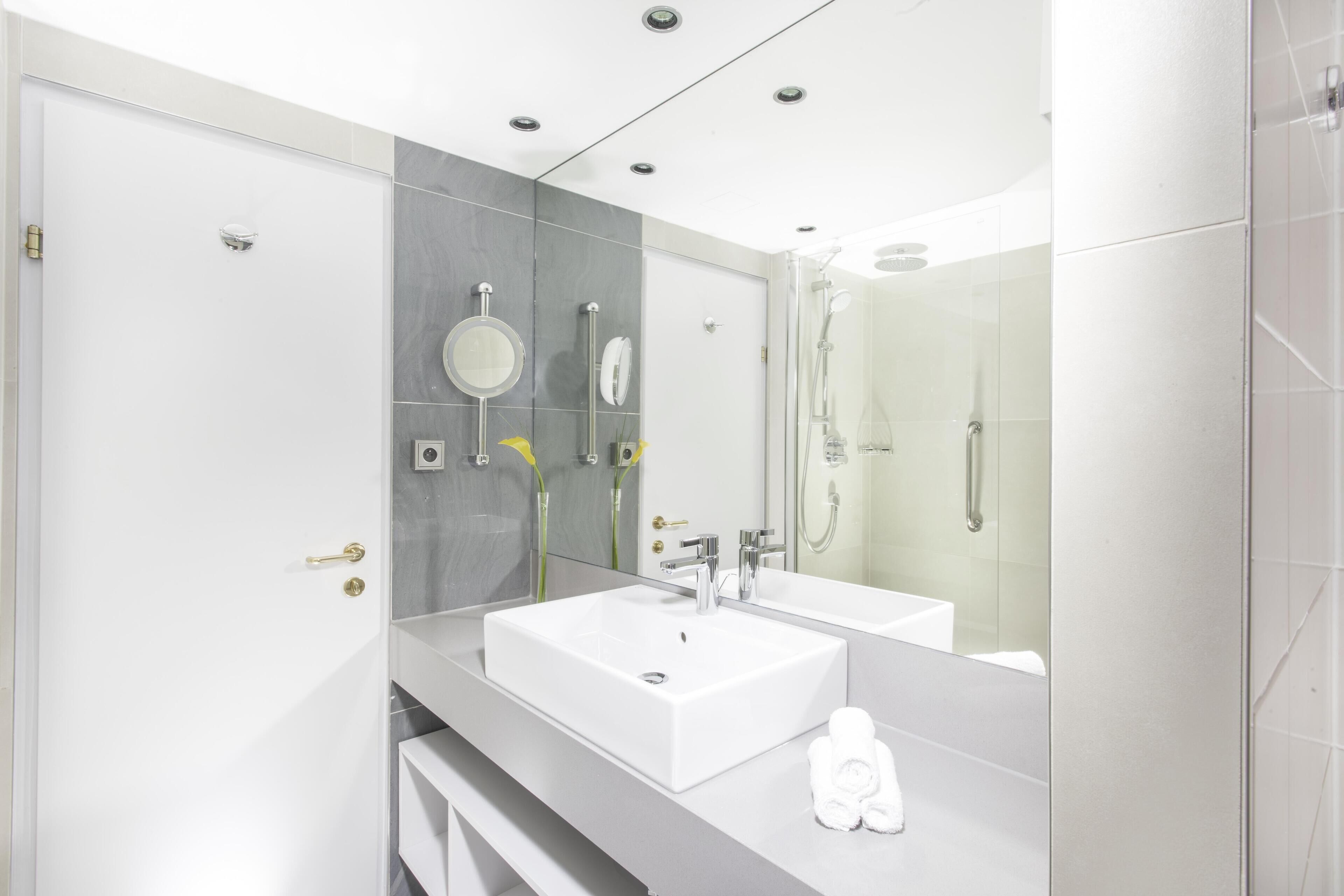Un bagno moderno con un lavandino capiente, uno specchio, una doccia e un water.