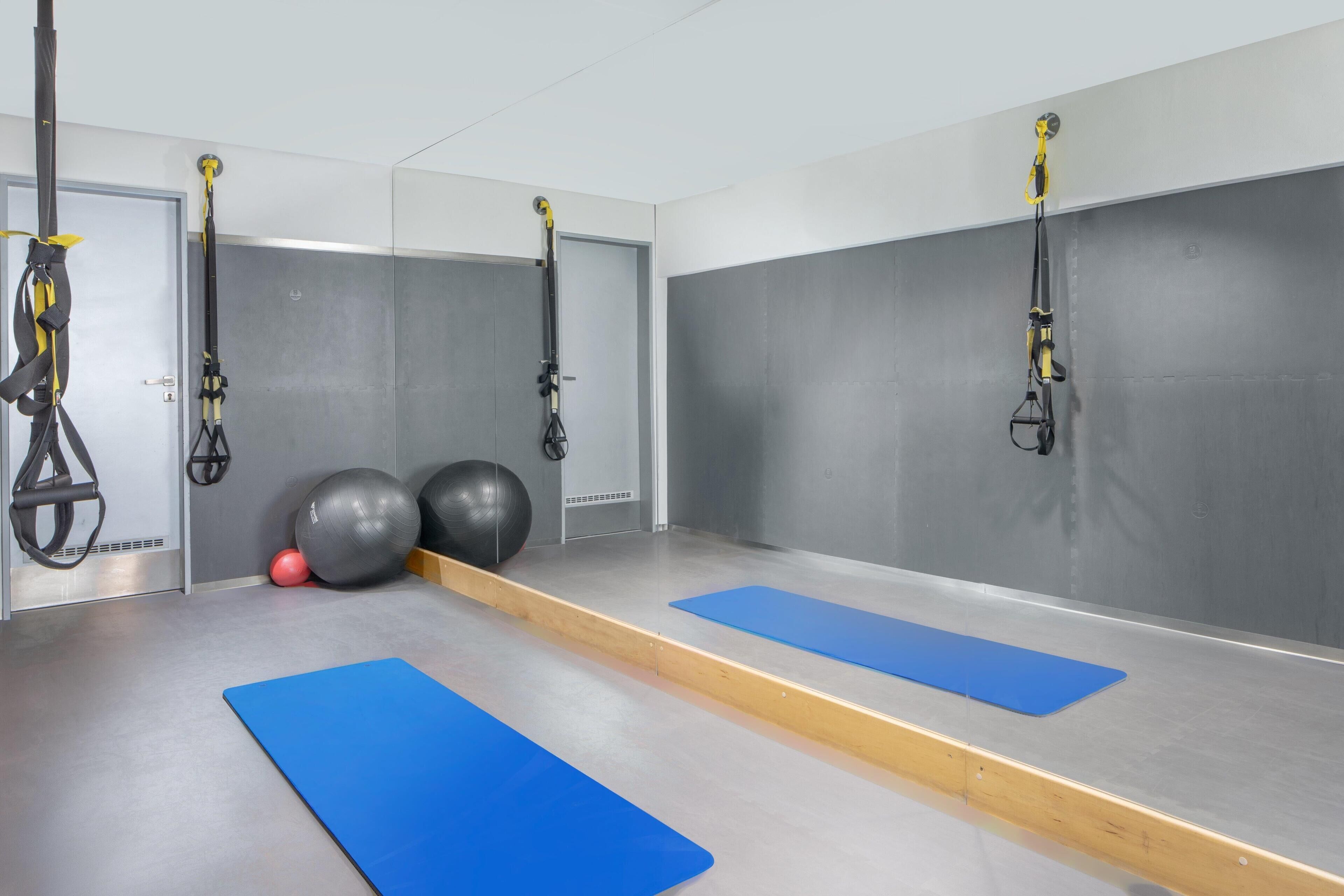 Academia com colchonetes azuis, bolas de exercício e aparelhos TRX.