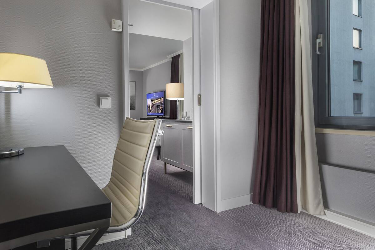 Habitación de hotel con cama, escritorio, silla, televisión y ventana con cortinas.
