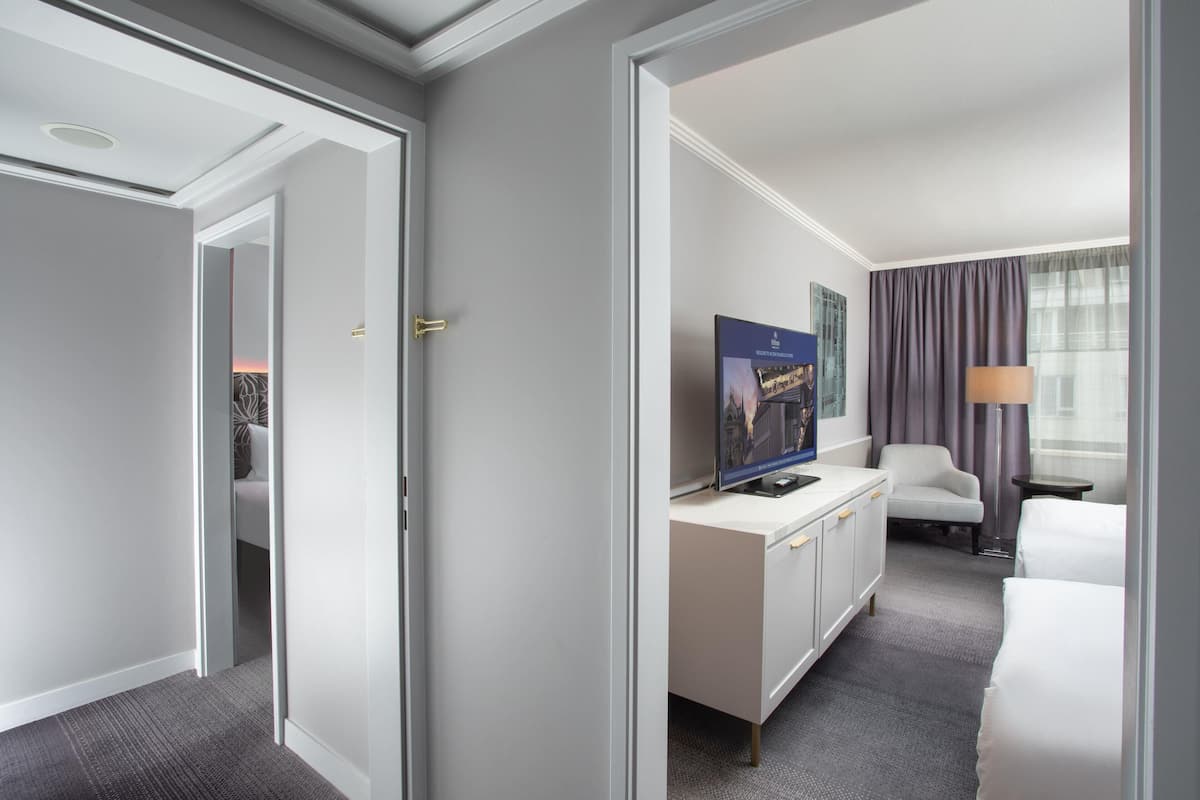 Habitación de hotel con cama, escritorio con televisor, silla y ventana con cortinas.