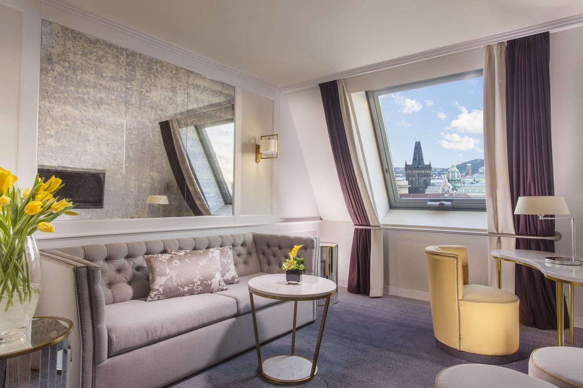 Una habitación de hotel moderna con un sofá, mesas redondas y un amplio ventanal con vista a la ciudad.