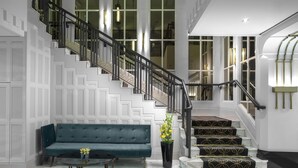 A grand staircase with a black railing, a blue sofa, and a vase with yellow flowers. - Hilton Prague Old Town (Prague)