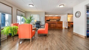 A modern interior with wooden flooring, orange chairs, a potted plant, and a kitchen area in the background. - Days Inn by Wyndham International Falls (International Falls)