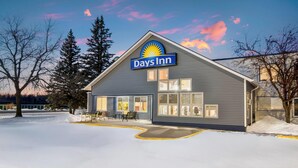A Days Inn hotel with a large sign, a covered outdoor seating area, and a snow-covered parking lot. - Days Inn by Wyndham International Falls (International Falls)