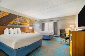 A hotel room with two beds, a desk, a chair, a TV, and a large painting on the wall. - Days Inn by Wyndham International Falls (International Falls)