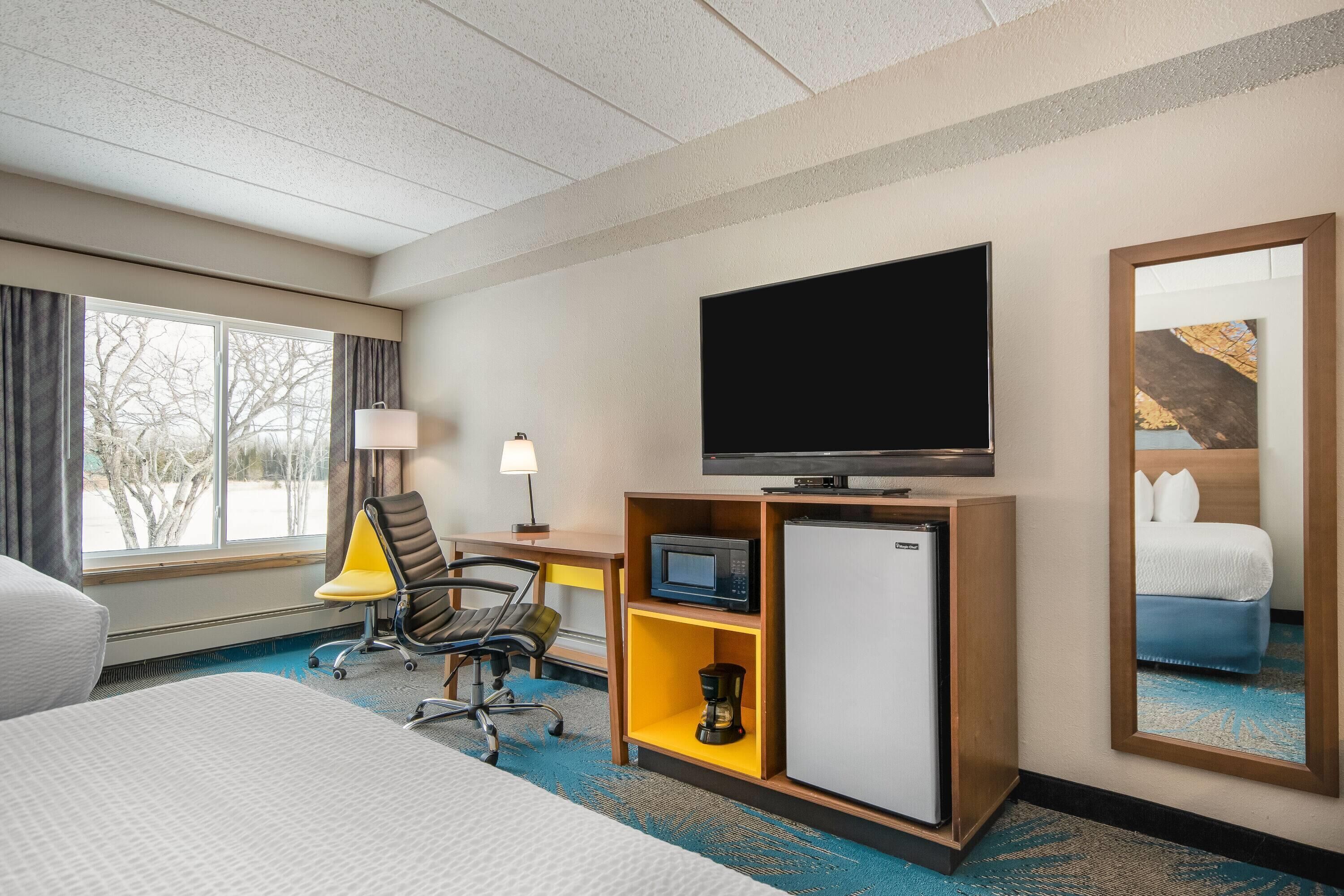 A hotel room with a bed, a desk with a lamp, a television, a microwave, a coffee maker, and a refrigerator.