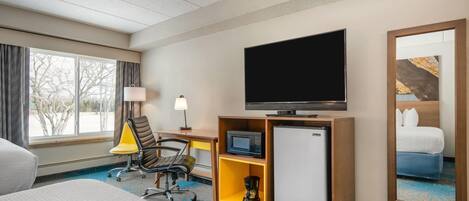 Una habitación de hotel con una cama, un escritorio con lámpara, televisión, microondas, cafetera y refrigerador.