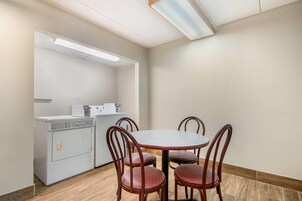 A small, clean room with a round table and four chairs, a washing machine, and a ceiling light fixture.