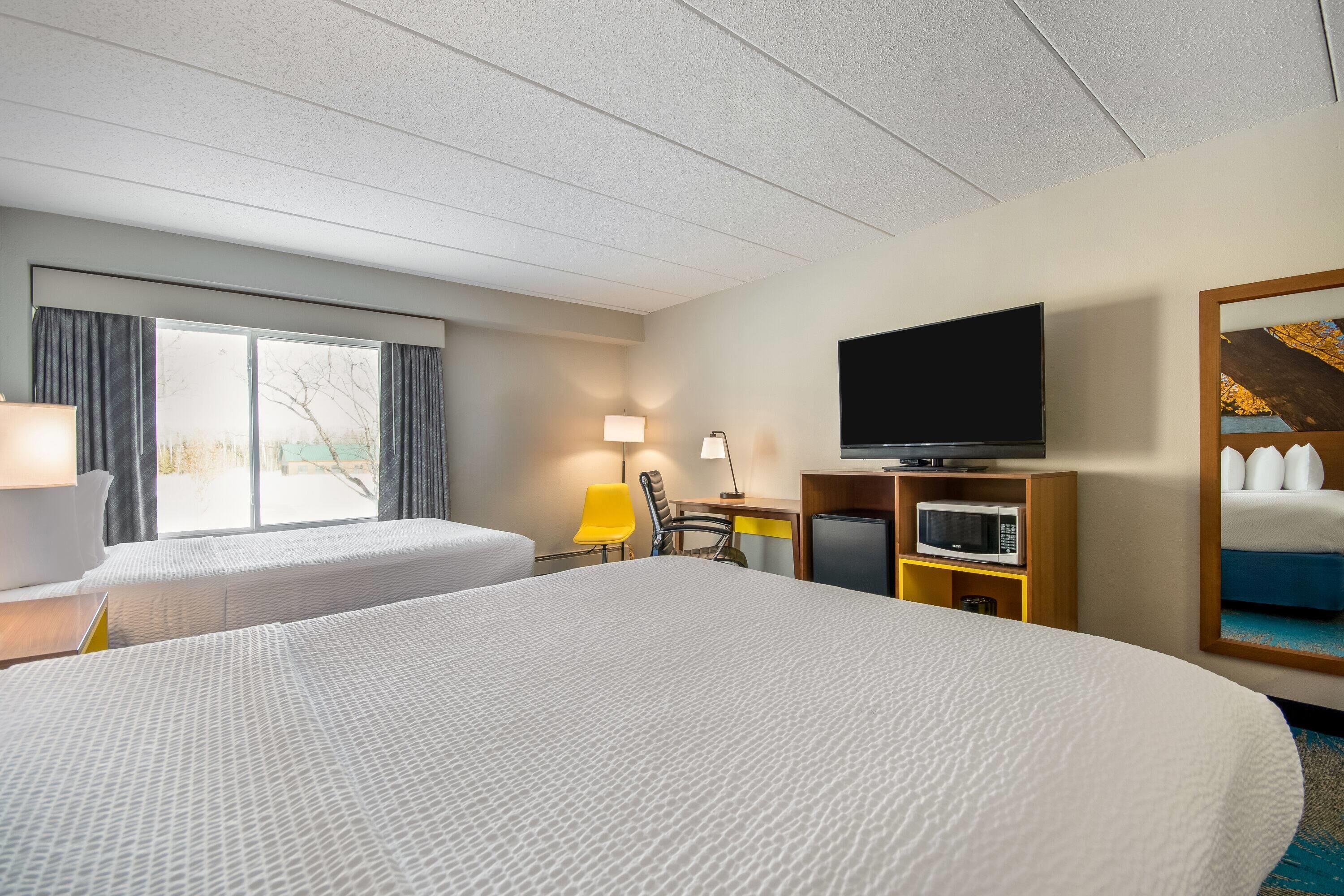 A hotel room with two beds, a desk, a television, and a window with curtains.